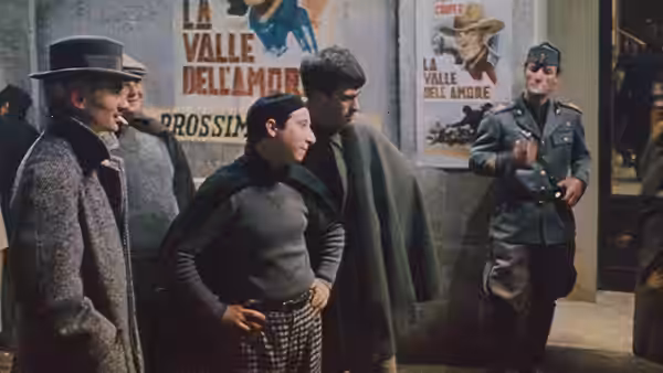 Men gathered near posters on a street wall with a soldier nearby