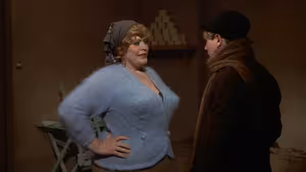 A woman in a blue sweater speaking with a man wearing a beret