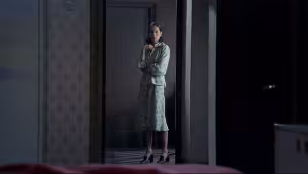 María (Geraldine Chaplin) stands in a doorway, clutching her hands in a dim room