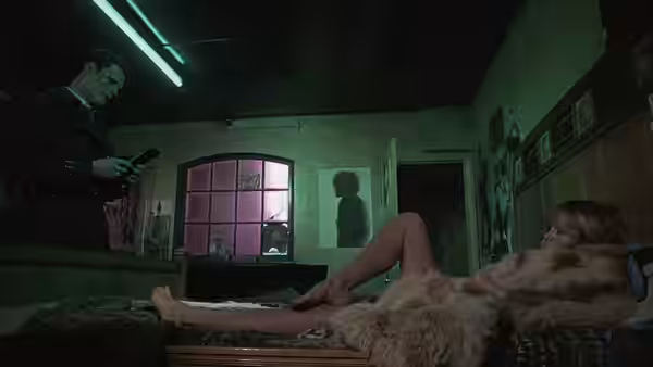 A man checks his phone near a woman reclining on a bed in fur