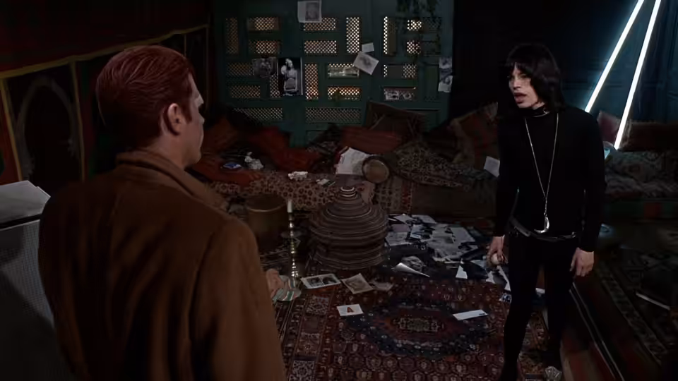 Chas (James Fox) faces Turner (Mick Jagger) in a room scattered with cards