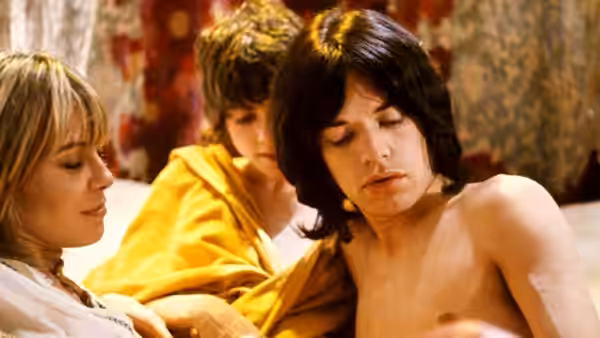 Turner (Mick Jagger) lies shirtless in bed between two companions