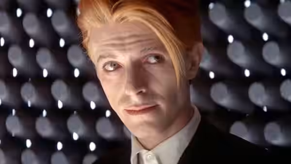Thomas Jerome Newton (David Bowie) with pale makeup glancing sideways against lights