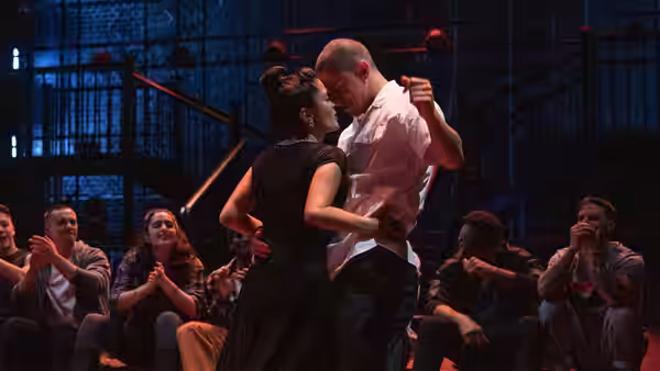 a man and woman embrace closely while slow dancing as spectators clap
