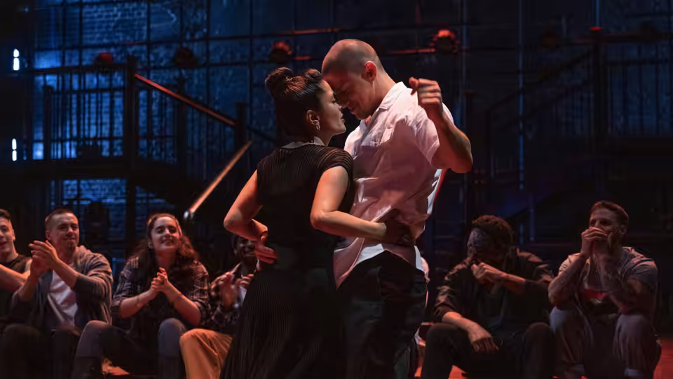 a man and woman embrace closely while slow dancing as spectators clap