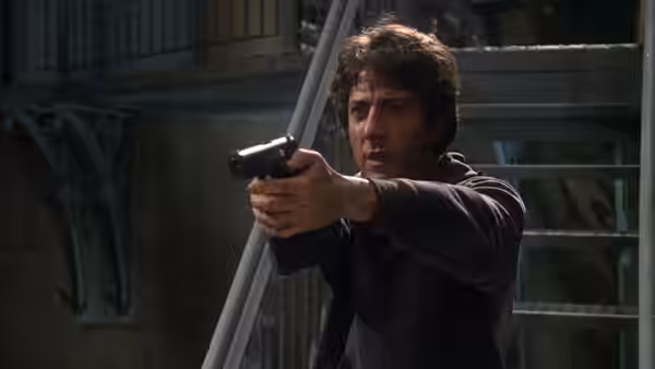 Thomas 'Babe' Levy (Dustin Hoffman) aiming a handgun forward on a metal staircase