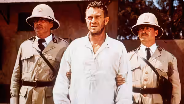 Papillon (Steve McQueen) held by two officers in pith helmets outside