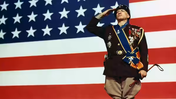 General Patton saluting while holding a riding crop before an American flag