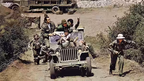 Soldiers piled on a jeep waving while others run alongside on a dirt road