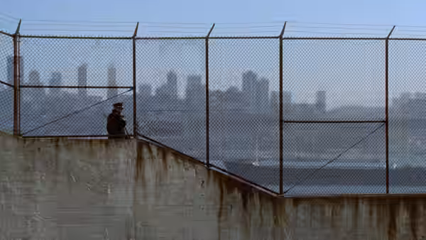 A prisoner stands by the fence on Alcatraz, with San Francisco across the water