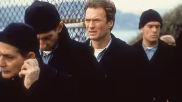 Frank Morris (Clint Eastwood) walks among prisoners in dark coats and caps
