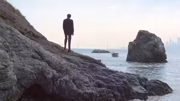Frank Morris (Clint Eastwood) stands on rocky shore, facing the water beyond Alcatraz