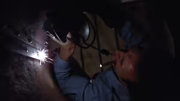 A prisoner welds metal inside a dim workshop