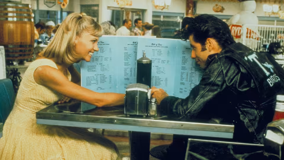 Sandy (Olivia Newton-John) smiles across the table at Danny (John Travolta)