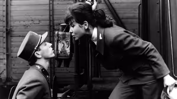 Milos Hrma (Václav Neckář) sits beside a railway carriage as a woman leans toward him