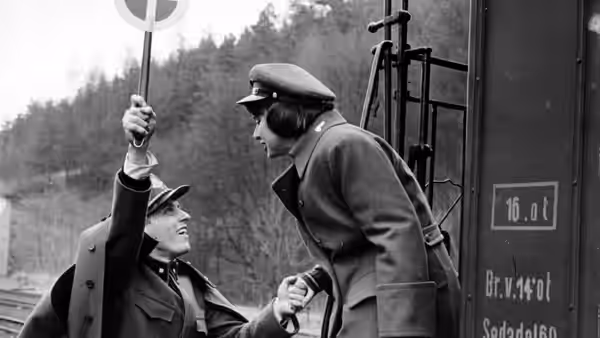 A uniformed railway worker and a seated man clasp hands beside a station platform