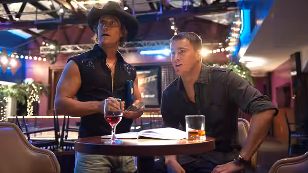 Dallas (Matthew McConaughey) and Mike (Channing Tatum) seated at a table with drinks