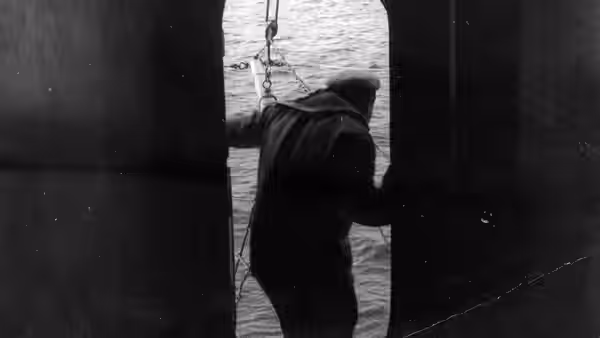 A sailor leans through a ship's open porthole above the water
