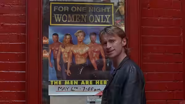 Guy (Hugo Speer) stands before a women-only show poster on a red door
