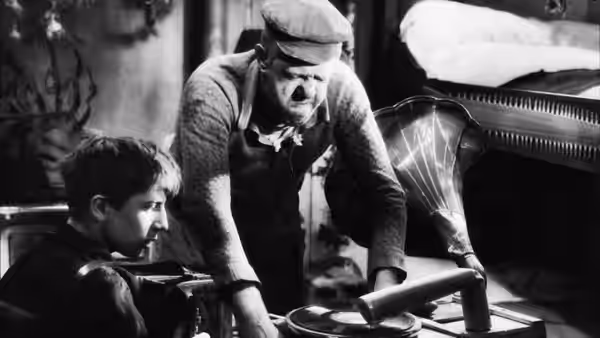 Père Jules (Michel Simon) bends over a gramophone as the cabin boy watches