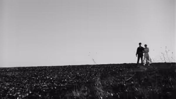 A couple stands together on a broad, empty stretch of shore