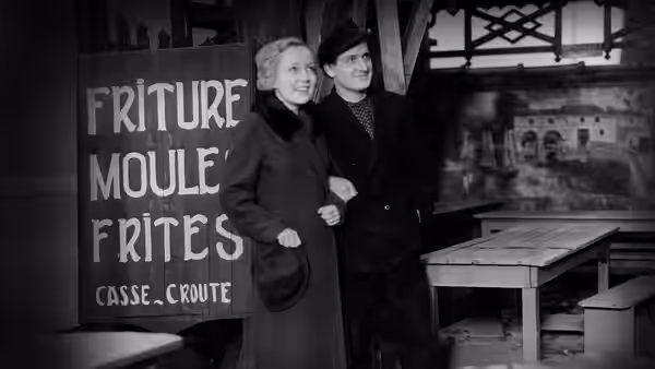 Juliette (Dita Parlo) stands beside a man in a beret inside a shop
