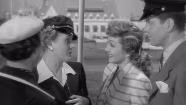 A woman in a cap talks with a smiling woman beside a uniformed man on a train