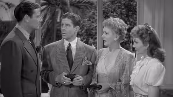 A suited man speaks with another man and two women holding small cases outdoors