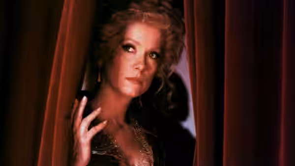 An actress parts the red curtains and looks toward the stage