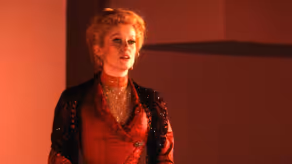 An actress stands under warm stage lights in a red costume