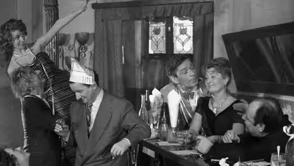 Guests gather around a hotel bar as a woman raises her arm