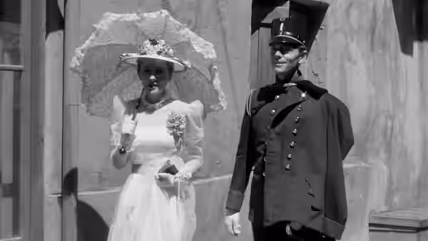 Lisa Berndle (Joan Fontaine) holds a parasol beside a uniformed officer outdoors