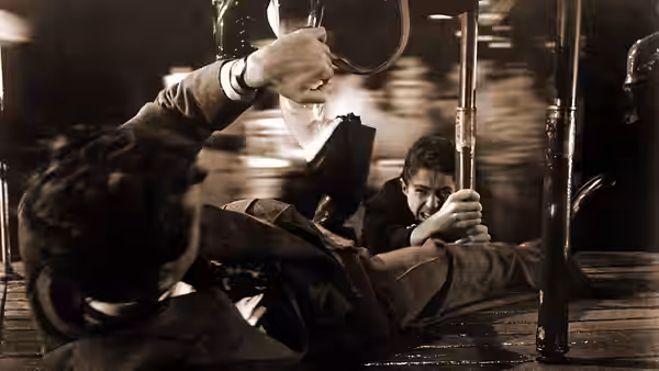 Two men struggle on a wet carousel platform during a confrontation
