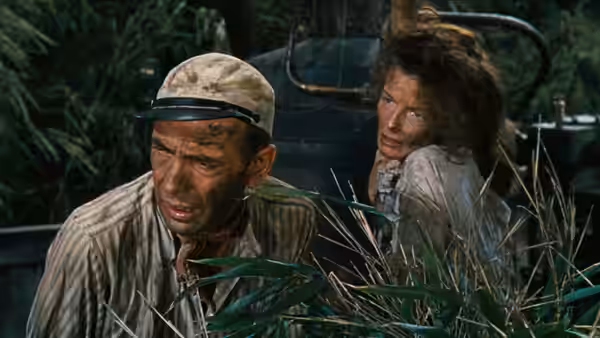 Charlie Allnut (Humphrey Bogart) looking ahead with Rose Sayer (Katharine Hepburn) hidden behind reeds