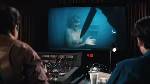 Two men watching a large screen displaying a woman in a shower with a knife