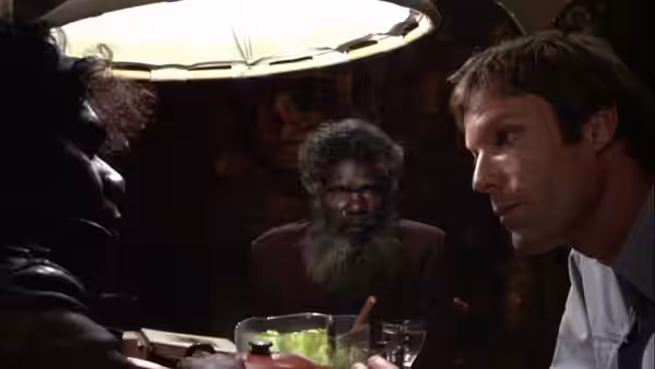 David Burton (Richard Chamberlain) listens across a table to an older bearded man