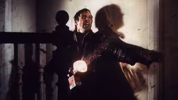 David Burton (Richard Chamberlain) recoils beside a staircase as a shadow looms behind him