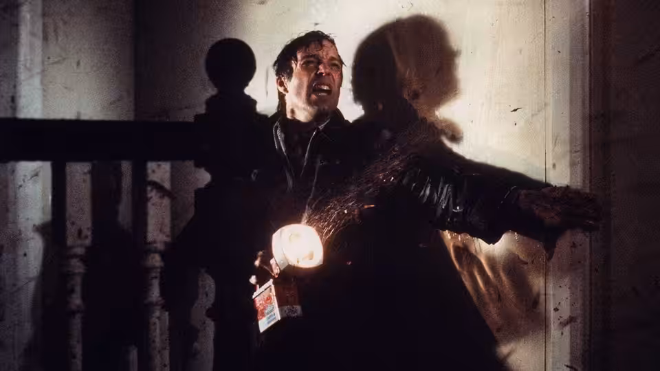 David Burton (Richard Chamberlain) recoils beside a staircase as a shadow looms behind him