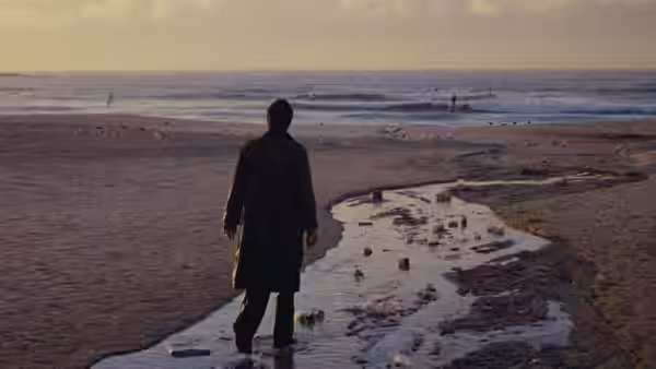 David Burton (Richard Chamberlain) stands at the shore beside a stream of water