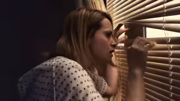 Sawyer Valentini (Claire Foy) peering through window blinds in a dark room