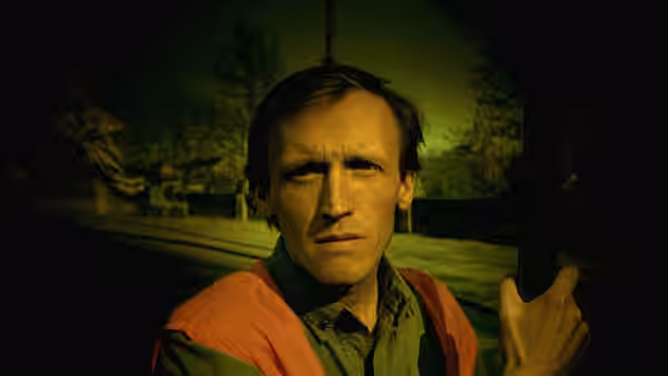 Man in orange safety vest gripping railing outdoors at night