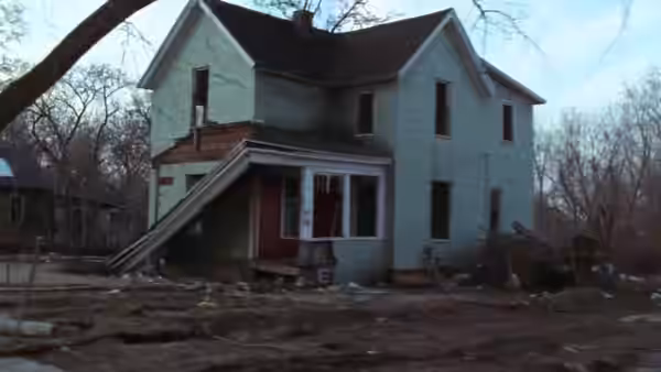 A two-story house with light green siding and a damaged front porch