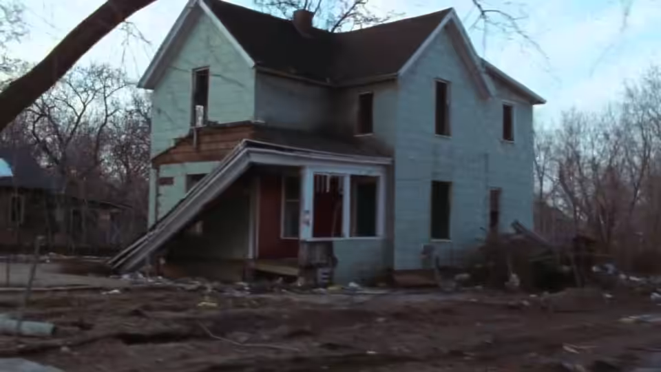 A two-story house with light green siding and a damaged front porch