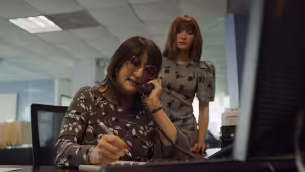 Woman speaking on the phone at her desk with a colleague nearby