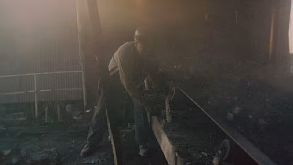 a miner in a hard hat working on machinery in a dark industrial space