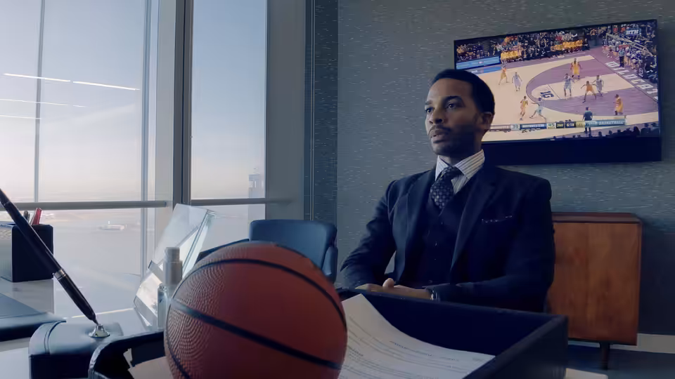 Ray Burke (André Holland) seated at an office desk with a basketball