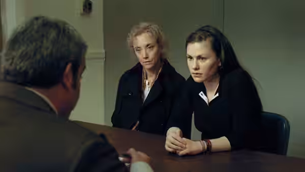 Two women sit at a wooden table facing a man in a suit