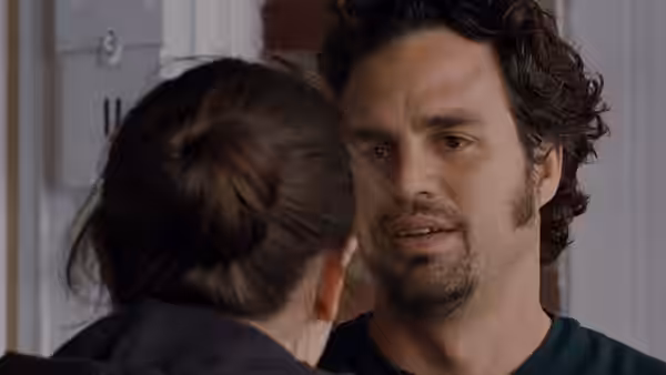Man with curly hair and beard talks closely to a woman seen from behind