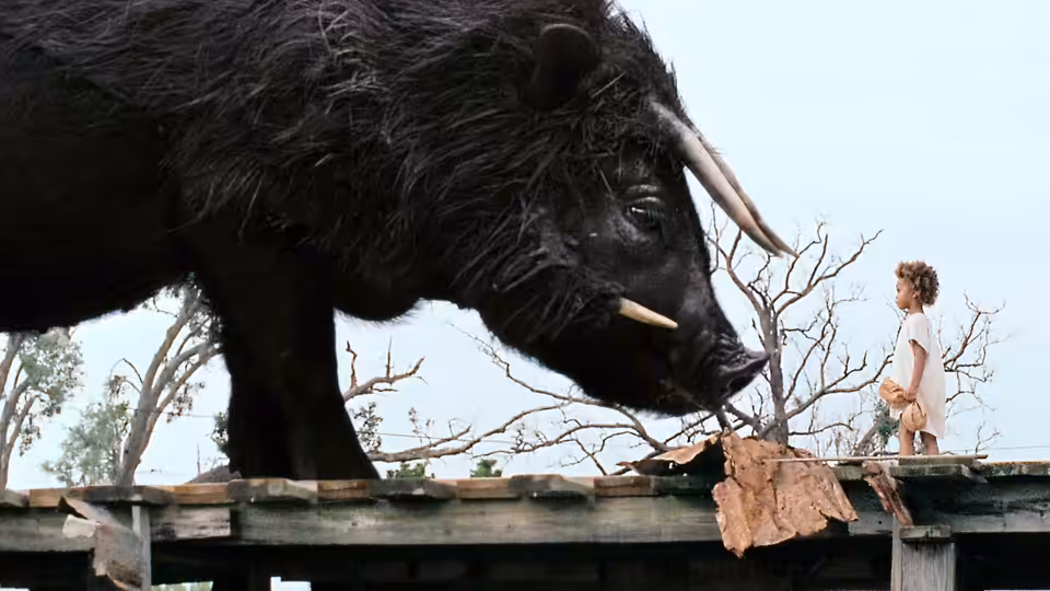 Hushpuppy facing a large black boar on a wooden platform
