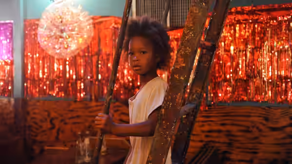 Hushpuppy holding a pole in a room with red tinsel curtains